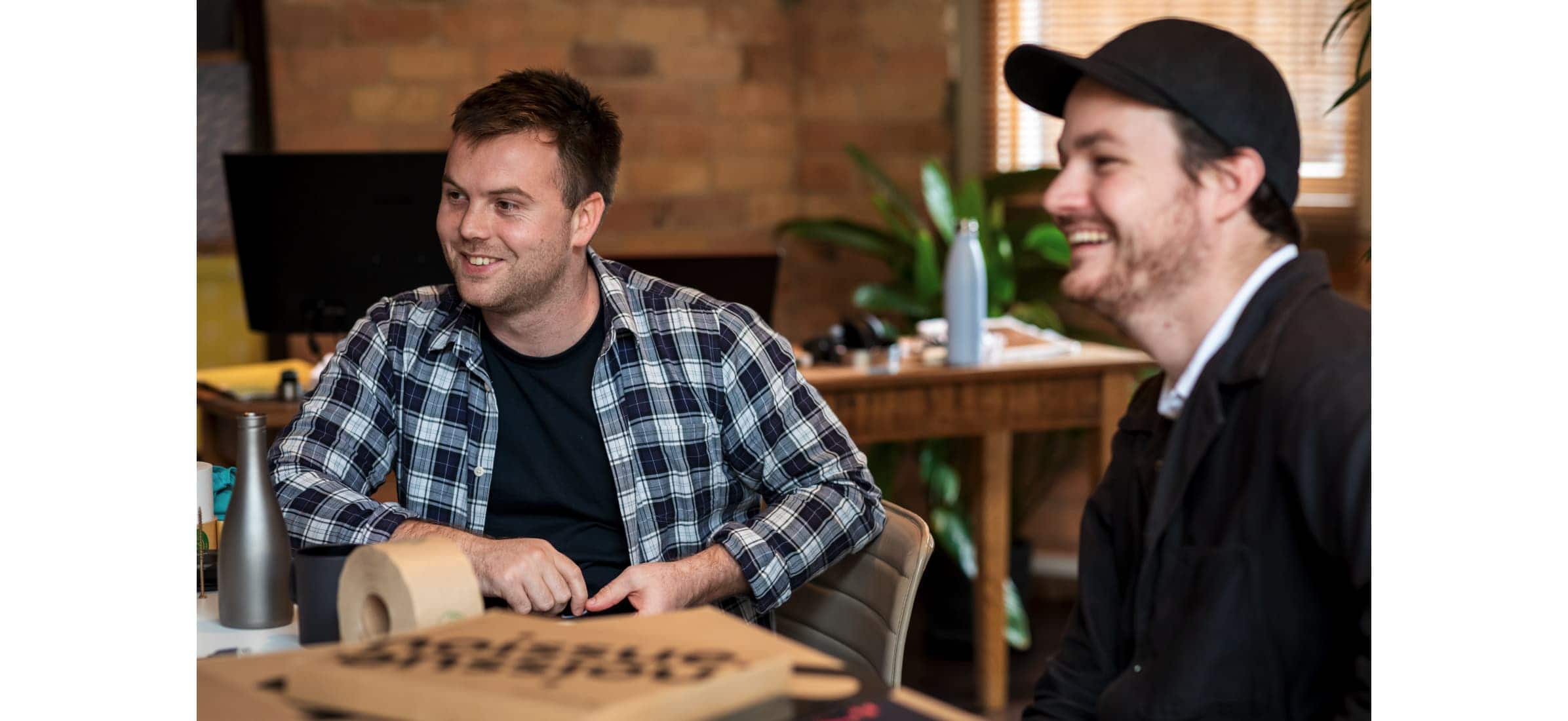 noissue company founders Josh Bowden and Augie Gruar smiling at a table in their office. 